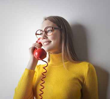 woman in yellow sweater holding red telephone