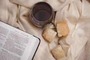 a glass of wine and bread pieces near a bible